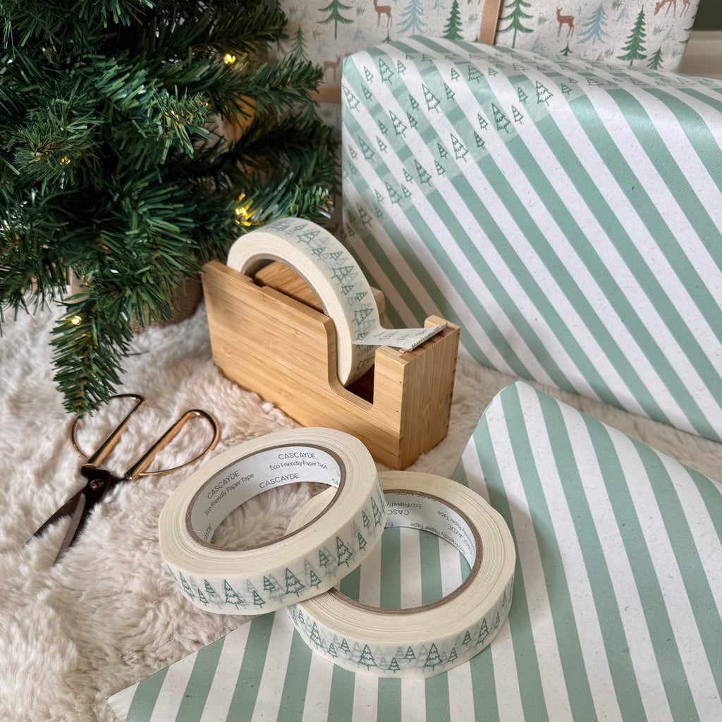 Decorative tape with tree pattern on a wooden dispenser and striped paper next to a Christmas tree.