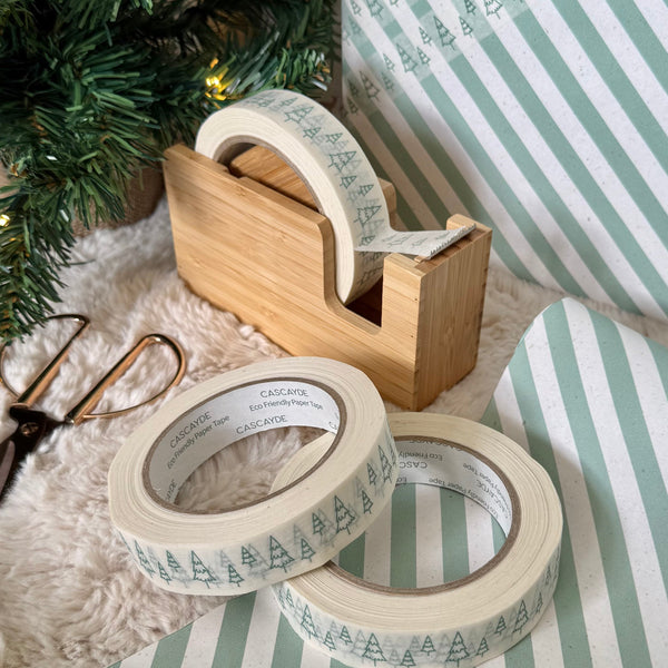 Decorative tape with tree pattern on a wooden dispenser and striped paper next to a Christmas tree.