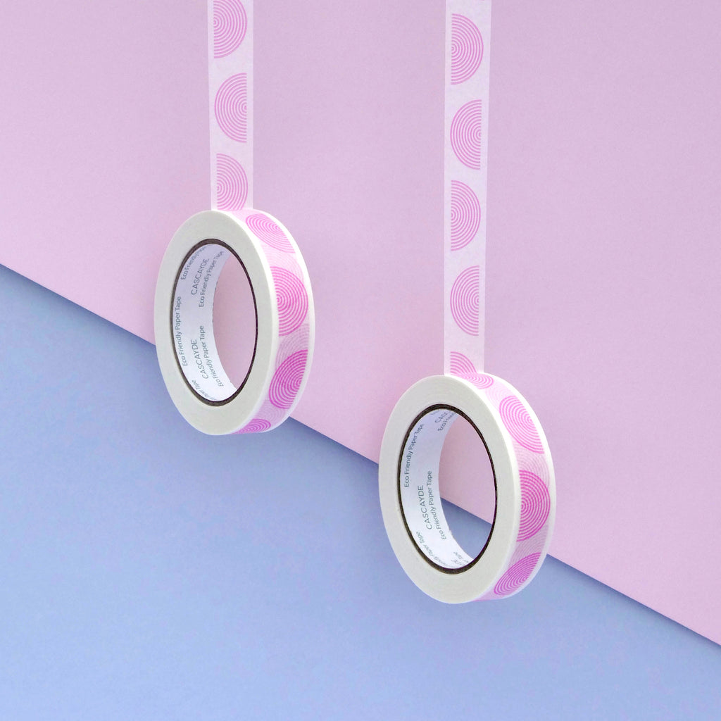 Two rolls of washi tape with a pink and white semicircle pattern, hanging against a split pastel pink and light blue background.
