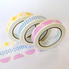 Three rolls of washi tape with pastel patterns, including yellow suns, blue stars, and pink semicircles, arranged on a white background with more of the patterned tape unrolled in front.