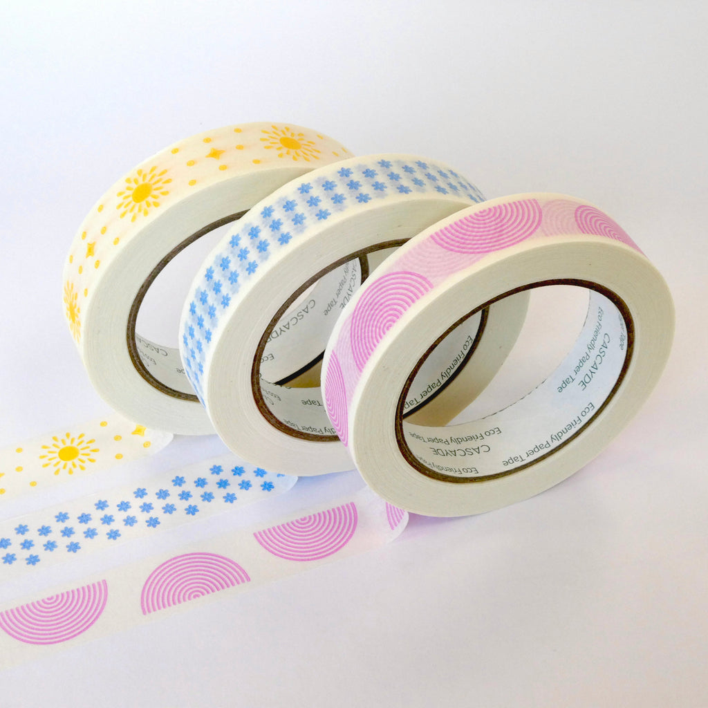 Three rolls of washi tape with pastel patterns, including yellow suns, blue stars, and pink semicircles, arranged on a white background with more of the patterned tape unrolled in front.