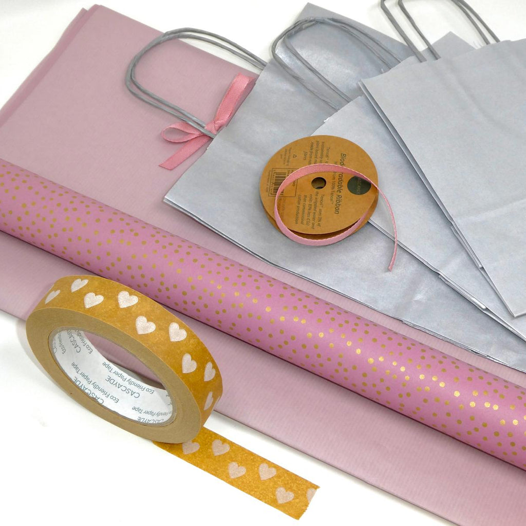 Pink wrapping paper, silver gift bag, and yellow tape with heart designs on a white background