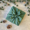 a gift wrapped in green furoshiki material gift wrap surrounded by pine cones