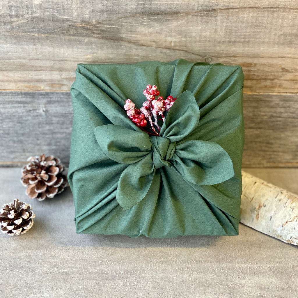 a gift wrapped in green furoshiki material gift wrap decorated with red berries  surrounded by pine cones