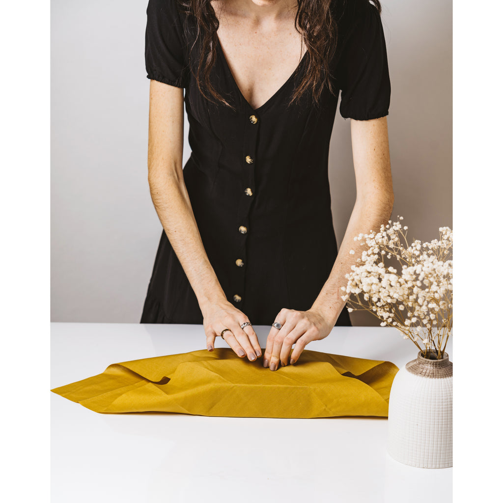 a tall lady in a black dress wraps a gift in yellow Furoshiki material gift wrap
