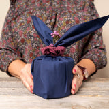 gift wrapped in navy blue Furoshiki material gift wrap on a table in front of a lady in a floral blouse 