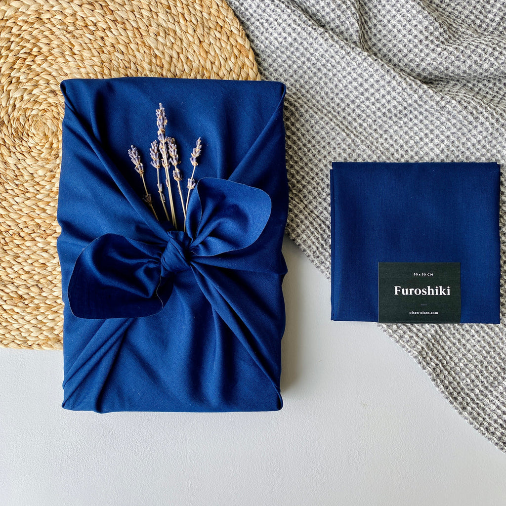 blue a gift wrapped in furoshiki material gift wrap surrounded by pine cones on top of a grey blanket