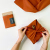 rust coloured furoshiki material gift wrap tied by hands with red nail polish