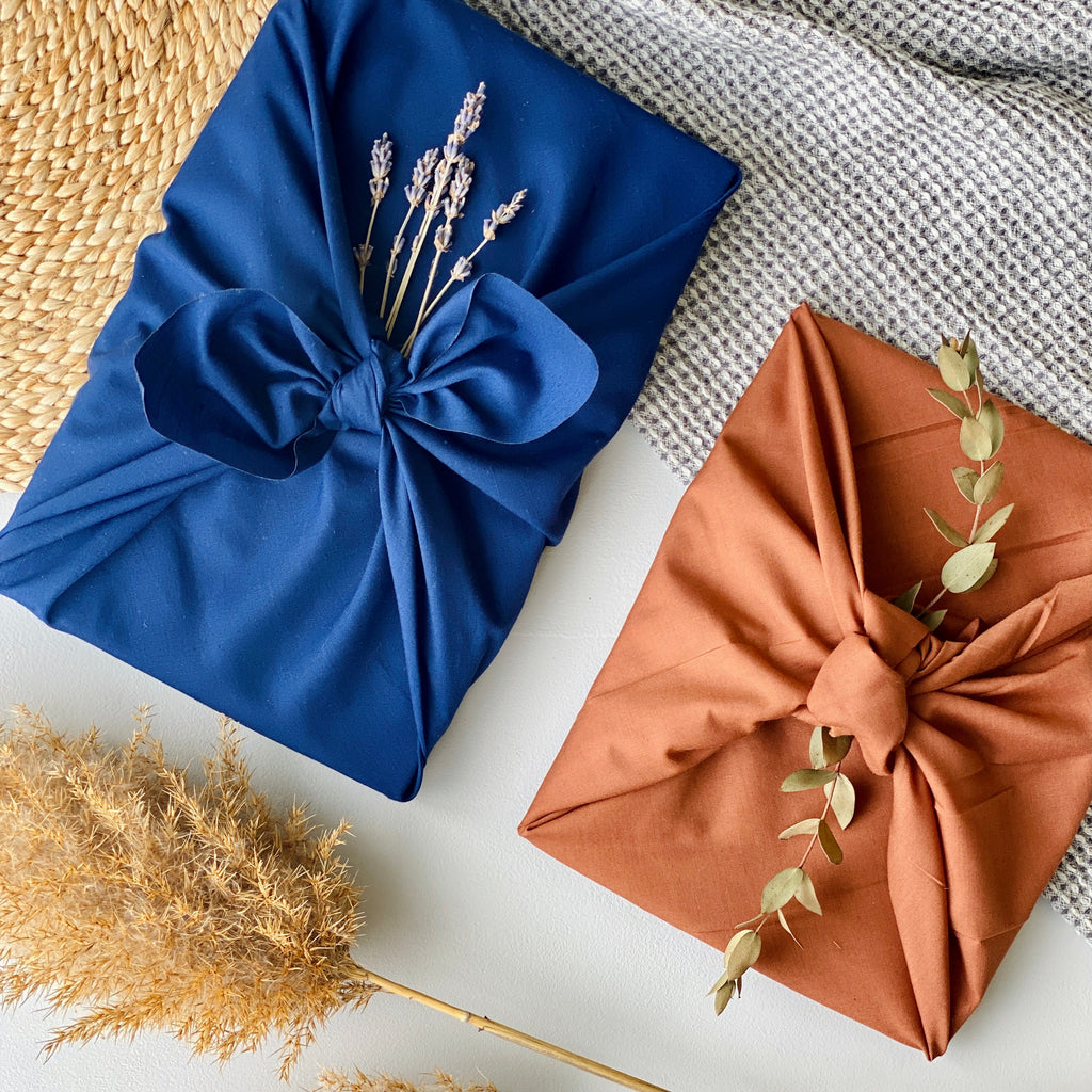 navy blue and rust coloured Furoshiki material gift wrap presents sit on a table next to dried leaves