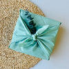 mint green furoshiki material gift wrap decorated with a dried leaf ontop of a wicker mat