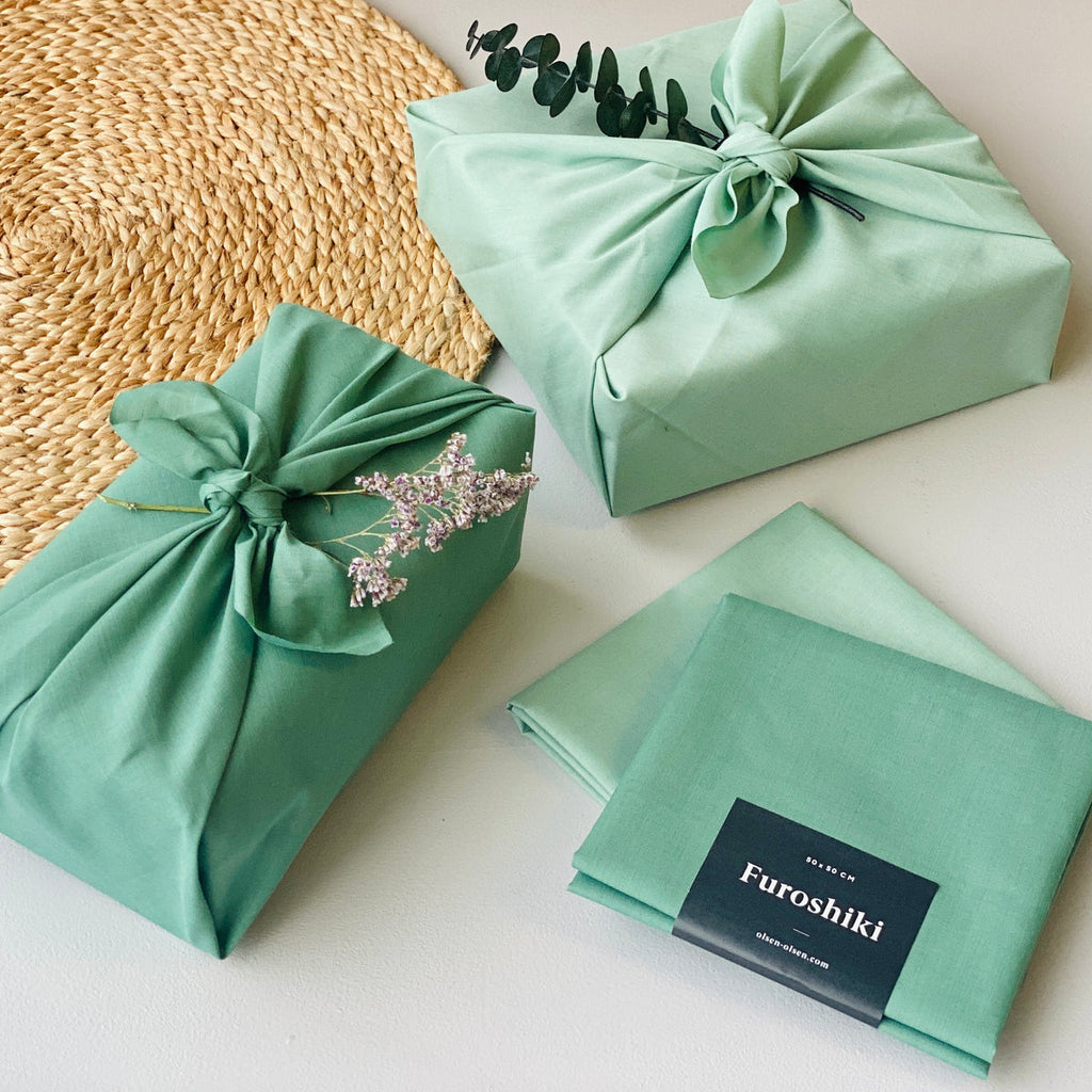 two green Furoshiki material gift wrapped presents next to another two folded on a table