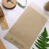 Grass paper mailing bag on a wood grain table with paper tape, ribbon and a fern leaf