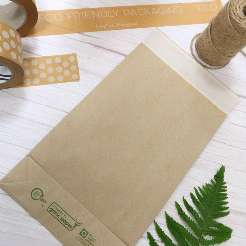 Grass paper mailing bag on a wood grain table with paper tape, ribbon and a fern leaf